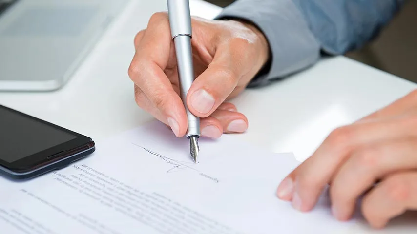 Hand signing a real estate contract on a desk