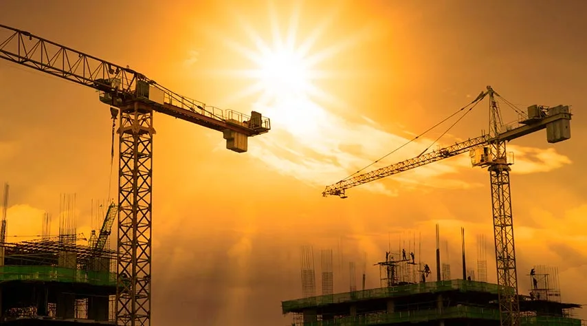 Tower cranes over buildings under construction at sunset