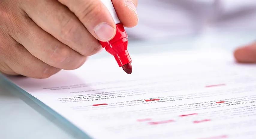 Hand marking up a property contract with a red pen during document review