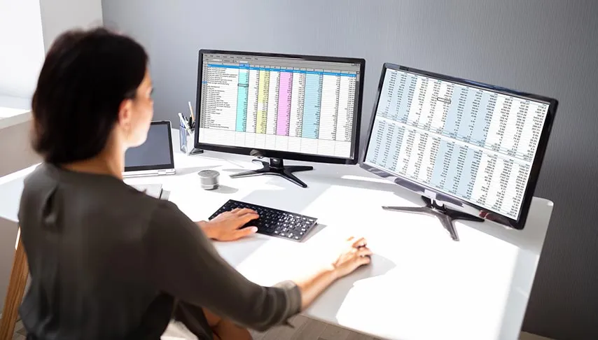 Analyst reviewing real estate data spreadsheets on dual monitors at a desk