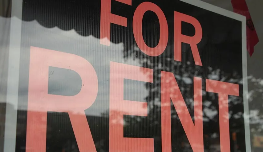 For rent sign in an apartment window reflecting the street outside